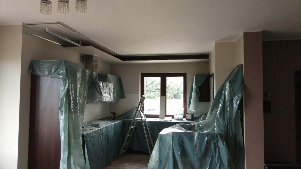 Przygotowanie kuchni do prac wykończeniowych w Koninie: meble i blaty zabezpieczone folią malarską, widoczna drabina i narzędzia, sufit z elementami konstrukcji pod płyty gipsowo-kartonowe.