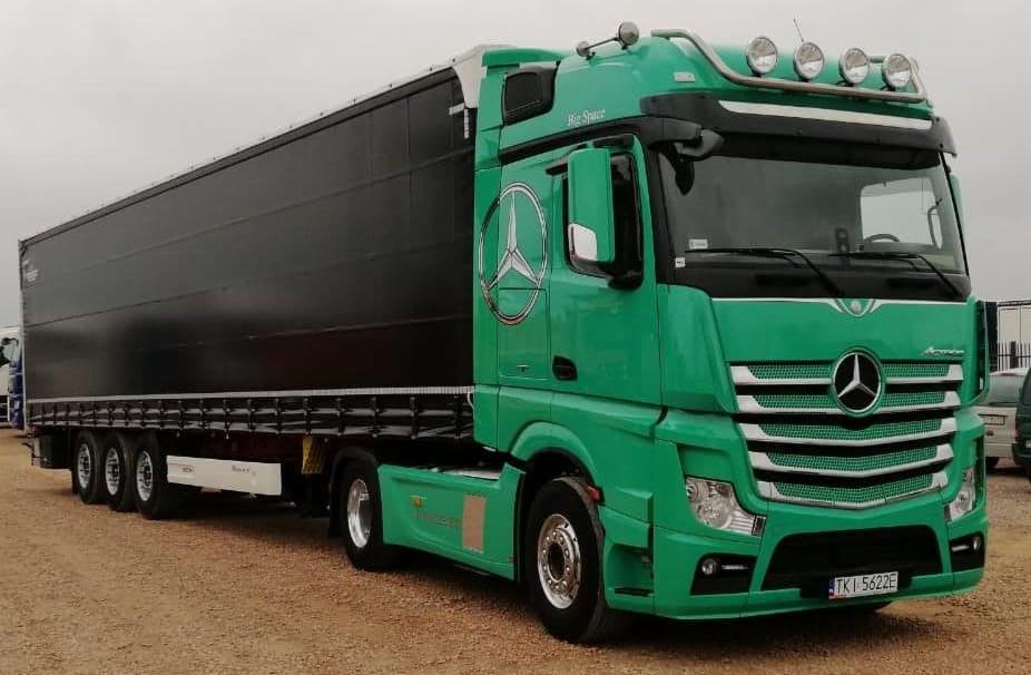 Zielony ciągnik siodłowy Mercedes-Benz Actros z naczepą, widok z boku na tle pochmurnego nieba, z widocznym logo firmy na kabinie i numerem rejestracyjnym TKI 5622E.