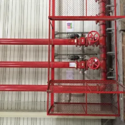 Czerwone rury i zawory w metalowej klatce ochronnej, instalacja przeciwpożarowa w hali przemysłowej.