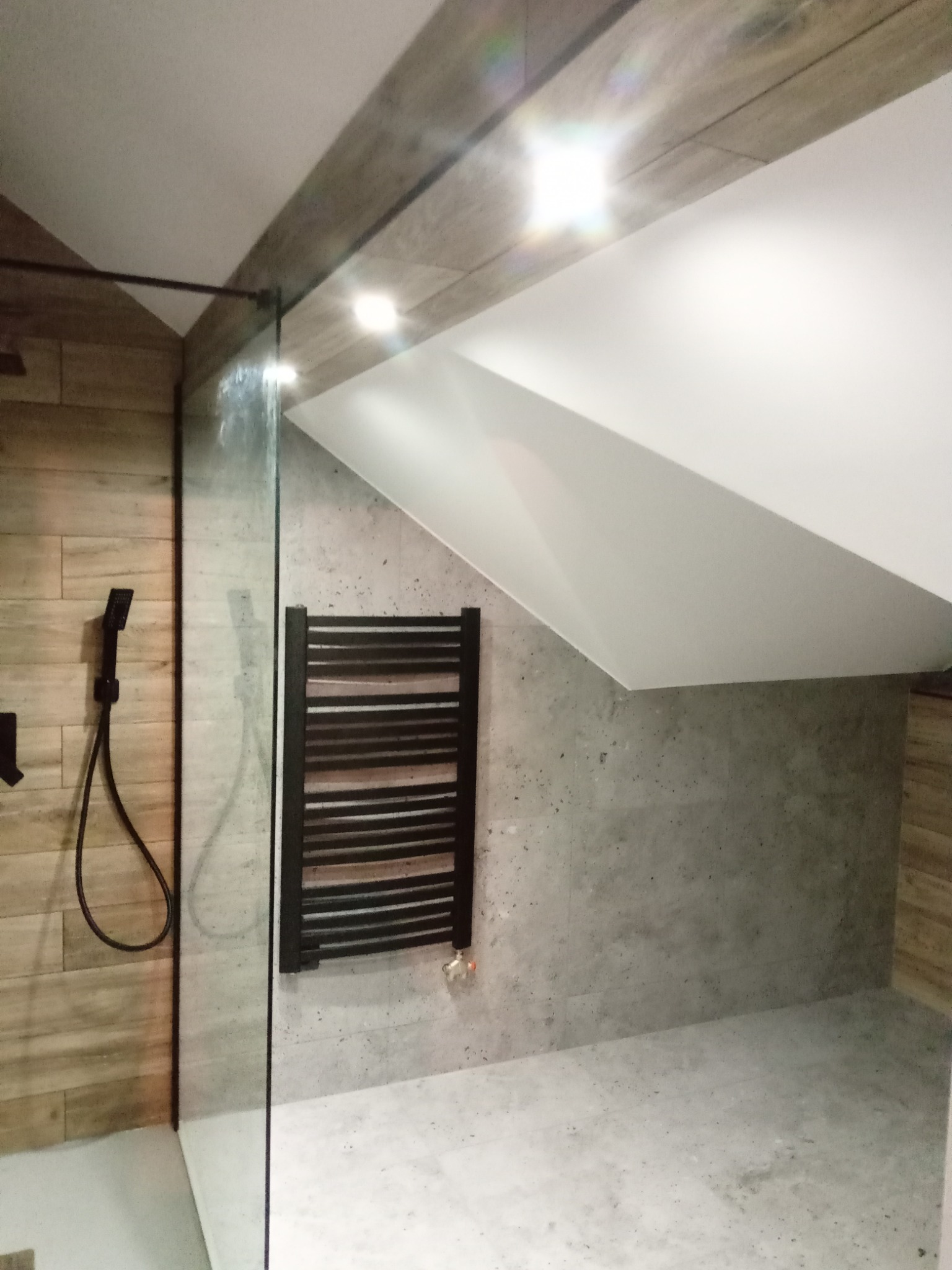 Nowoczesna łazienka w odcieniach szarości i drewna z kabiną prysznicową typu walk-in, grzejnikiem drabinkowym i skośnym sufitem.