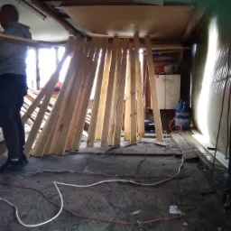 Przygotowanie do ocieplenia poddasza: widoczne drewniane elementy konstrukcyjne, butla gazowa, przewody i narzędzia na podłodze podczas prac montażowych.