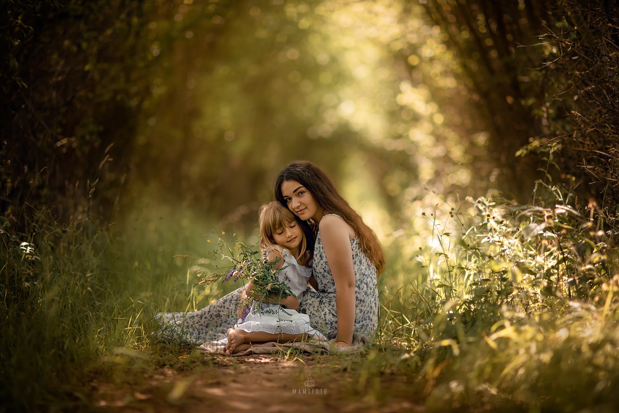Matka z córką siedząca na ścieżce w lesie, dziewczynka trzyma bukiet polnych kwiatów, ciepłe, naturalne światło.