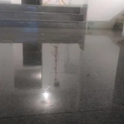 Błyszcząca, ciemna posadzka z płytek kamiennych odbija schody i elementy wnętrza, tworząc lustrzany efekt.