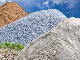 Góra żwiru, piasku i ziemi w Czudcu na tle błękitnego nieba. Różne frakcje kruszyw budowlanych ułożone warstwami, widoczne źdźbła trawy u podstawy.