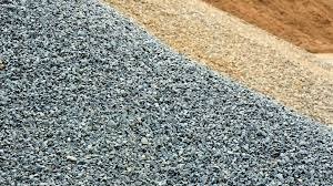 Góra drobnego, szarego kruszywa na tle beżowego piasku i brązowej ziemi. Widok z bliska, ukazujący teksturę materiałów.