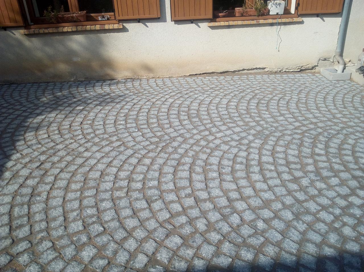 Ułożona kostka granitowa w kształcie wachlarza na podwórku domu jednorodzinnego, widoczne okna z brązowymi okiennicami i doniczkami z kwiatami.