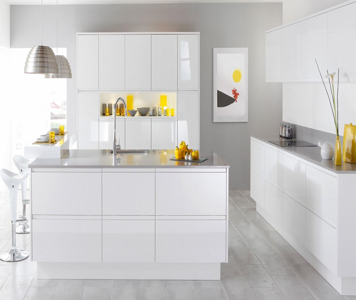Nowoczesna kuchnia z białymi, lakierowanymi frontami, wyspą z szarym blatem i chromowaną armaturą, oświetlona wiszącymi lampami i z akcentami w kolorze żółtym.