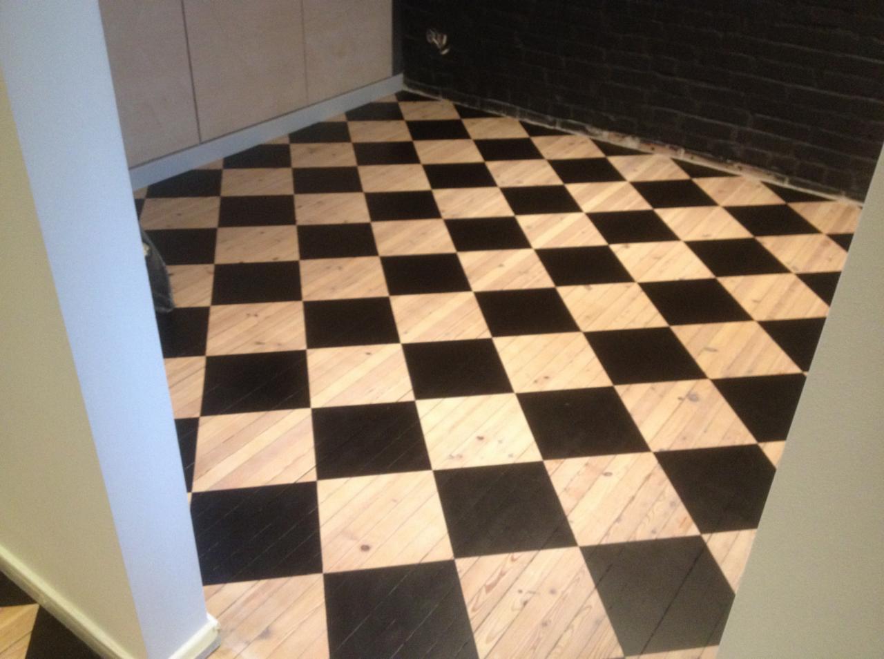 Podłoga w szachownicę z desek pomalowanych na czarno i naturalne drewno, widok z góry, fragment ściany z czarnej cegły w tle.