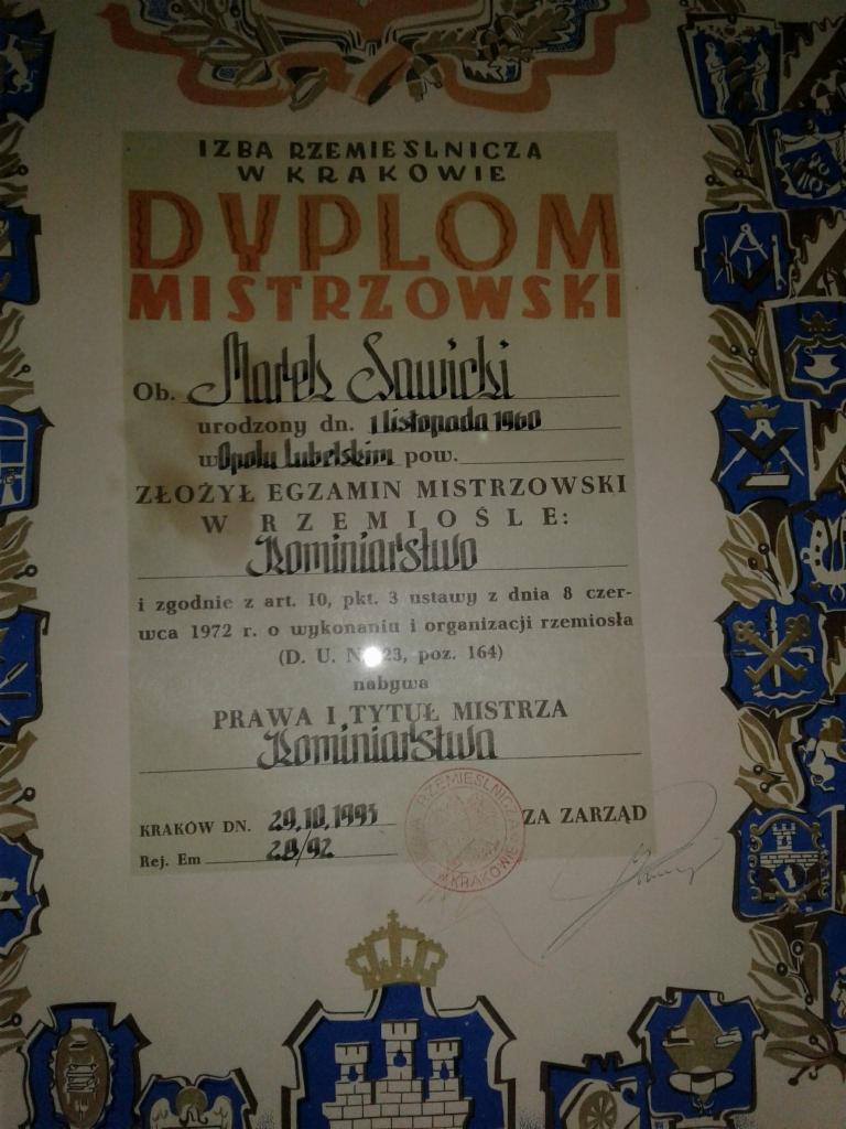 Skan dyplomu mistrzowskiego w rzemiośle kominiarskim, wydany w Krakowie w 1995 roku, oprawiony w ramkę z dekoracyjnymi herbami cechowymi.