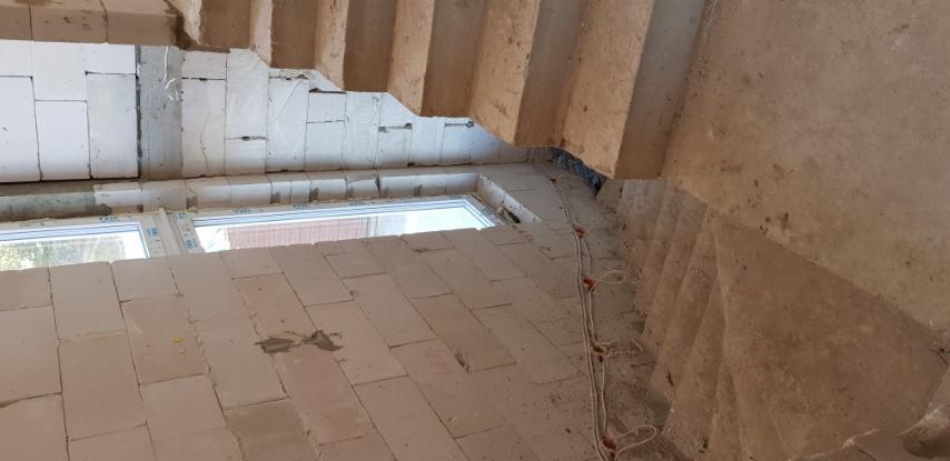 Wnętrze domu w trakcie przebudowy: widoczne murowane ściany z betonu komórkowego, okno wstawione w surowy mur oraz fragment betonowych schodów.