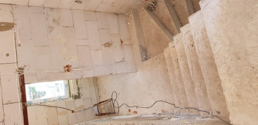 Wnętrze surowego domu w trakcie przebudowy: ściany z betonu komórkowego z widoczną instalacją elektryczną, okno PCV i surowe betonowe schody.