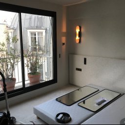 FACH-BUD firma remontowo-malarska - Nowoczesne wnętrze w trakcie remontu: widoczny odkurzacz Miele, przygotowane lustra do montażu na tle okna z widokiem na budynki z blachy falistej i rośliny w donicach.