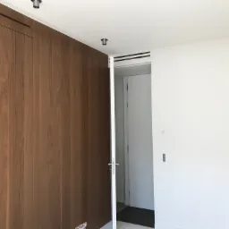 Wnętrze z drewnianą zabudową szafy wnękowej, białą ścianą i otwartymi drzwiami do kolejnego pomieszczenia z widoczną białą ścianą i podłogą.