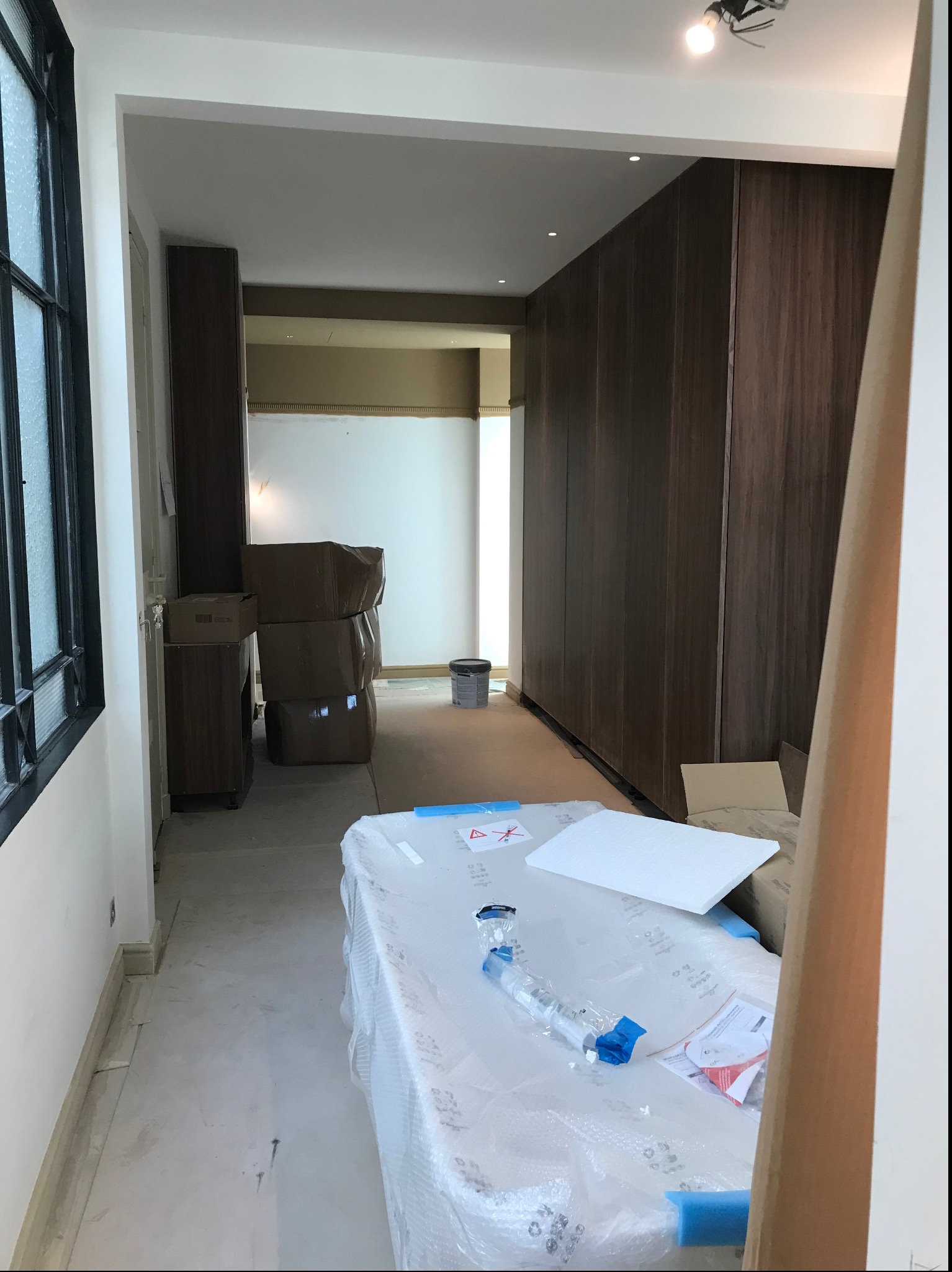 Wnętrze w trakcie prac wykończeniowych: widoczne kartony, zabezpieczona folią powierzchnia, ściany przygotowane do malowania, zabudowa meblowa w tle.