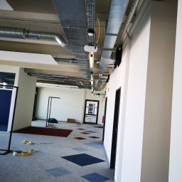Usługi Elektryczno Budowlane Leszek Drewczyński - Sufit z instalacjami wentylacyjnymi i elektrycznymi w biurze w Mostach. Widoczne koryta kablowe i rury wentylacyjne, surowy stan wykończenia wnętrza.