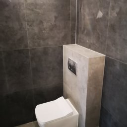 Usługi Elektryczno Budowlane Leszek Drewczyński - Nowoczesna łazienka z podwieszaną toaletą i szarą glazurą. Minimalistyczny design, widoczny przycisk spłukiwania. Wykończenie w odcieniach szarości.