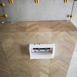 Usługi Elektryczno Budowlane Leszek Drewczyński - Ułożona glazura w jodełkę na ścianie z widoczną puszką instalacyjną i systemem poziomowania płytek. Detal wykończenia wnętrza łazienki w trakcie prac.