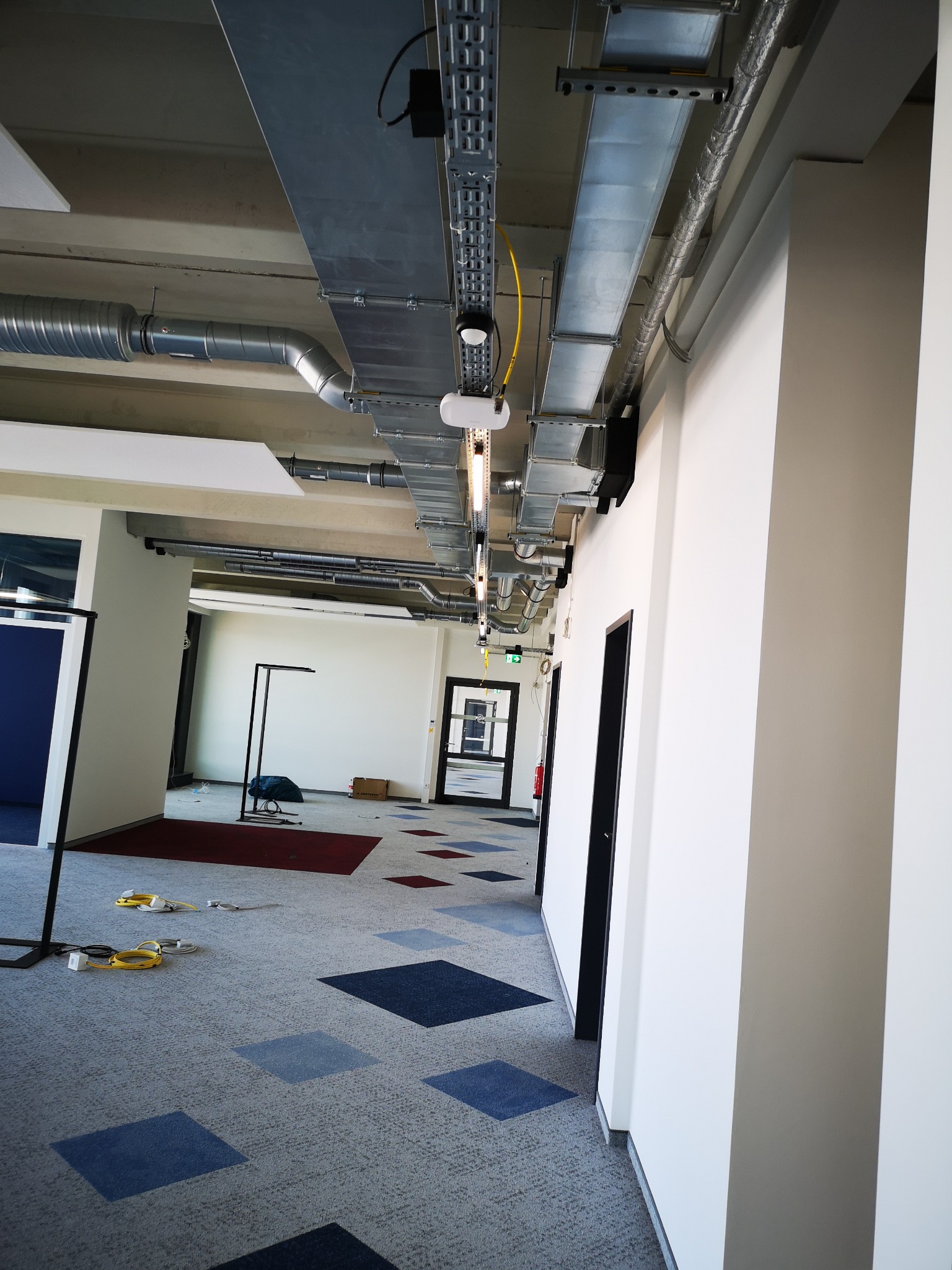 Sufit z instalacjami wentylacyjnymi i elektrycznymi w biurze w Mostach. Widoczne koryta kablowe i rury wentylacyjne, surowy stan wykończenia wnętrza.