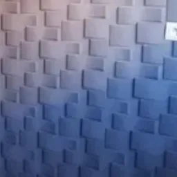 Ściana z dekoracyjnymi panelami 3D w odcieniach szarości i błękitu, oświetlona z g&oacute;ry, z widocznym gniazdkiem elektrycznym.