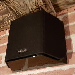 Agra Art Rafał Dogoda - Czarny głośnik Monitor Audio zamontowany na ceglanej ścianie pod drewnianą belką stropową.