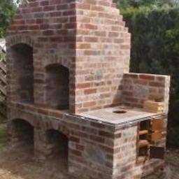 Dariusz Majak usługi zduńskie - Murowana konstrukcja z cegły z otworami paleniskowymi i kominem, widoczna na zewnątrz w ogrodzie, z elementami rusztu