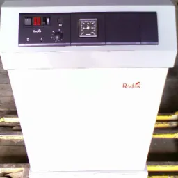 Kocioł gazowy żeliwny Radan RA 22 z widocznym panelem sterowania, manometrem i logotypem producenta na białej obudowie, ustawiony na palecie.