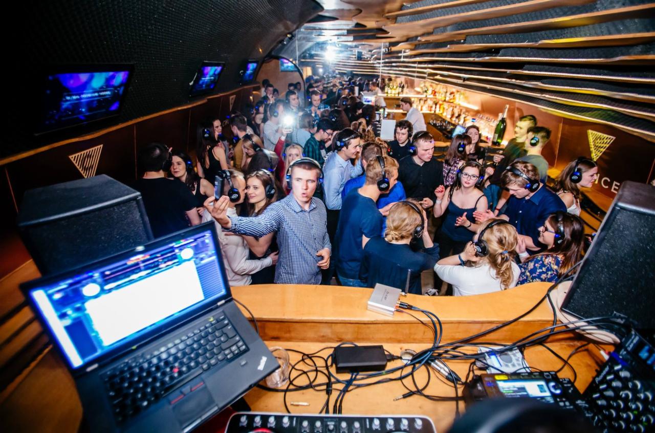 Silent disco: Grupa ludzi w klubie, tańczących w słuchawkach, z laptopem DJ-a i mikserem na pierwszym planie.