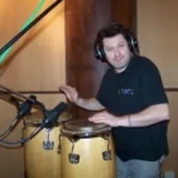 Mężczyzna w słuchawkach grający na bębnach conga w studiu nagraniowym, widoczne mikrofony.
