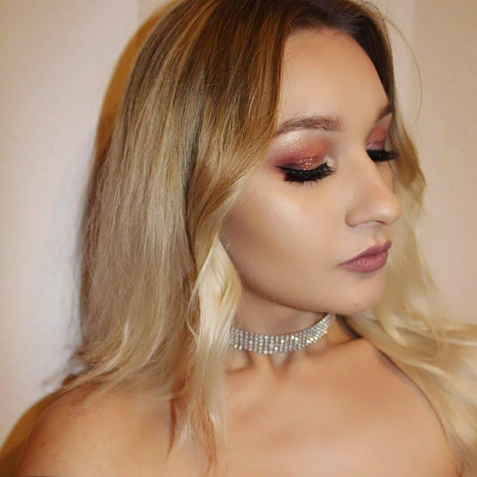 Portret kobiety z profesjonalnym makijażem oczu w odcieniach różu i błyszczącym brokatem, podkreślonym czarnym eyelinerem, oraz delikatnie podkreślonymi ustami w kolorze mauve, uzupełnionym...