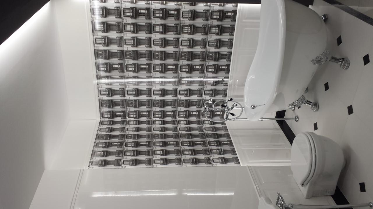 Wykończona łazienka w stylu retro z białą wolnostojącą wanną na ozdobnych nóżkach, toaletą oraz tapetą z motywem okiennic.