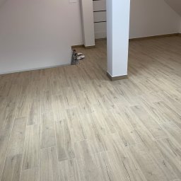 Firma Wielobranżowa Przemysław Rycharski - Poddasze po remoncie z ułożoną podłogą z płytek imitujących drewno, widoczne wystające kable elektryczne ze ściany.