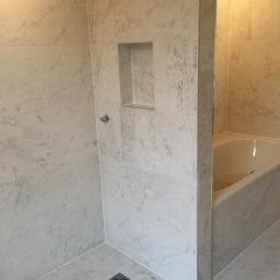 Firma Wielobranżowa Przemysław Rycharski - Wykończona łazienka z marmurowymi płytkami na ścianach i podłodze, wnęka w ścianie, widoczny fragment wanny.