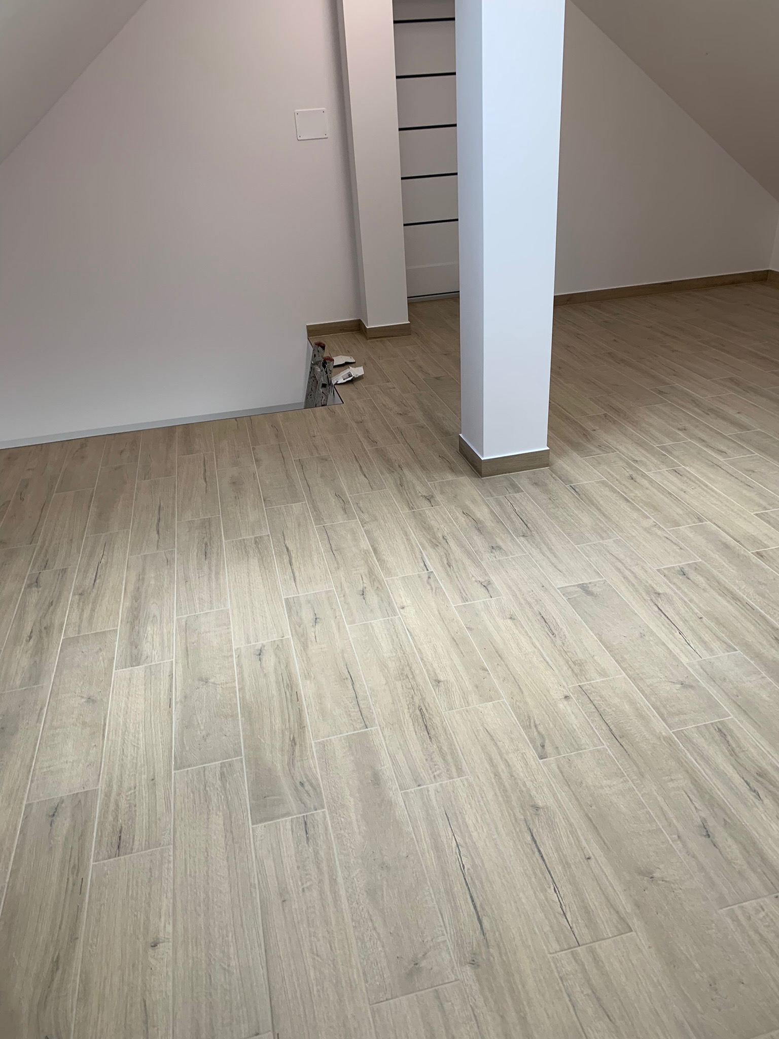 Poddasze po remoncie z ułożoną podłogą z płytek imitujących drewno, widoczne wystające kable elektryczne ze ściany.