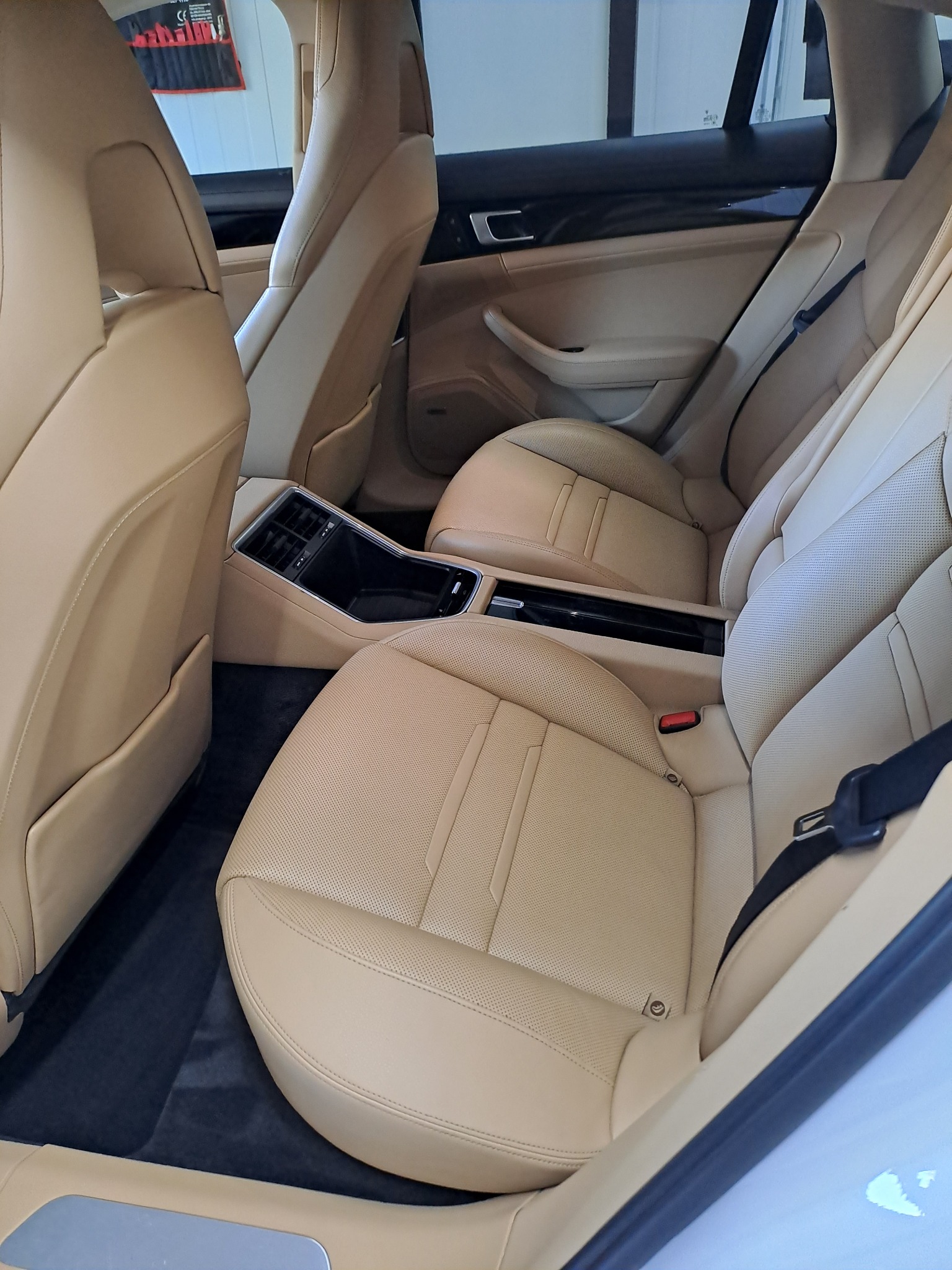 Beżowe skórzane fotele tylne Porsche Panamera z widoczną perforacją i czarnymi pasami bezpieczeństwa, czarna podłoga.