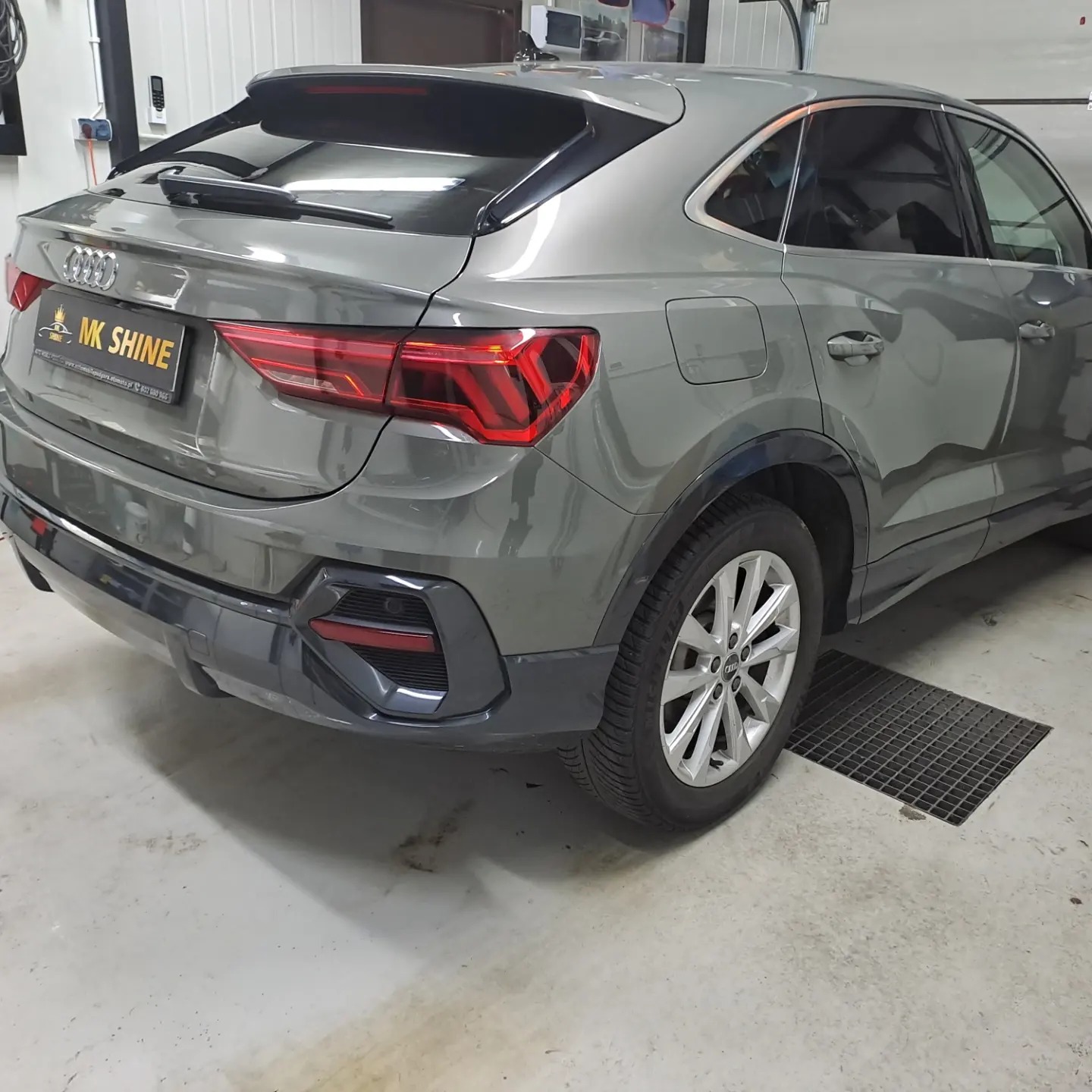 Szary Audi Q3 Sportback po usłudze myjni, widoczne logo MK Shine na tylnej klapie, w tle kratka ściekowa na posadzce.
