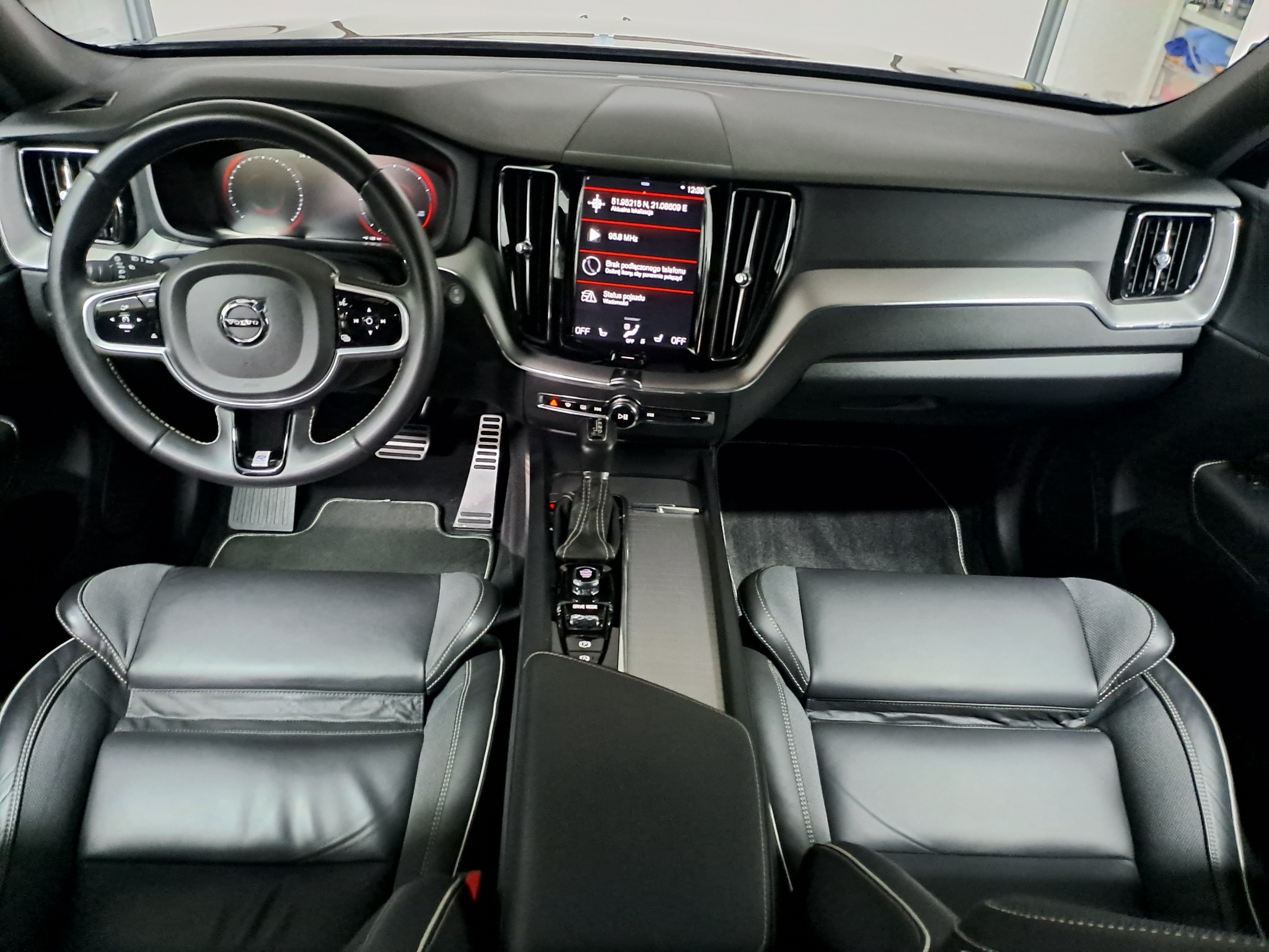 Wnętrze samochodu Volvo z czarną skórzaną tapicerką foteli, widok na deskę rozdzielczą, kierownicę i centralny panel z ekranem dotykowym.