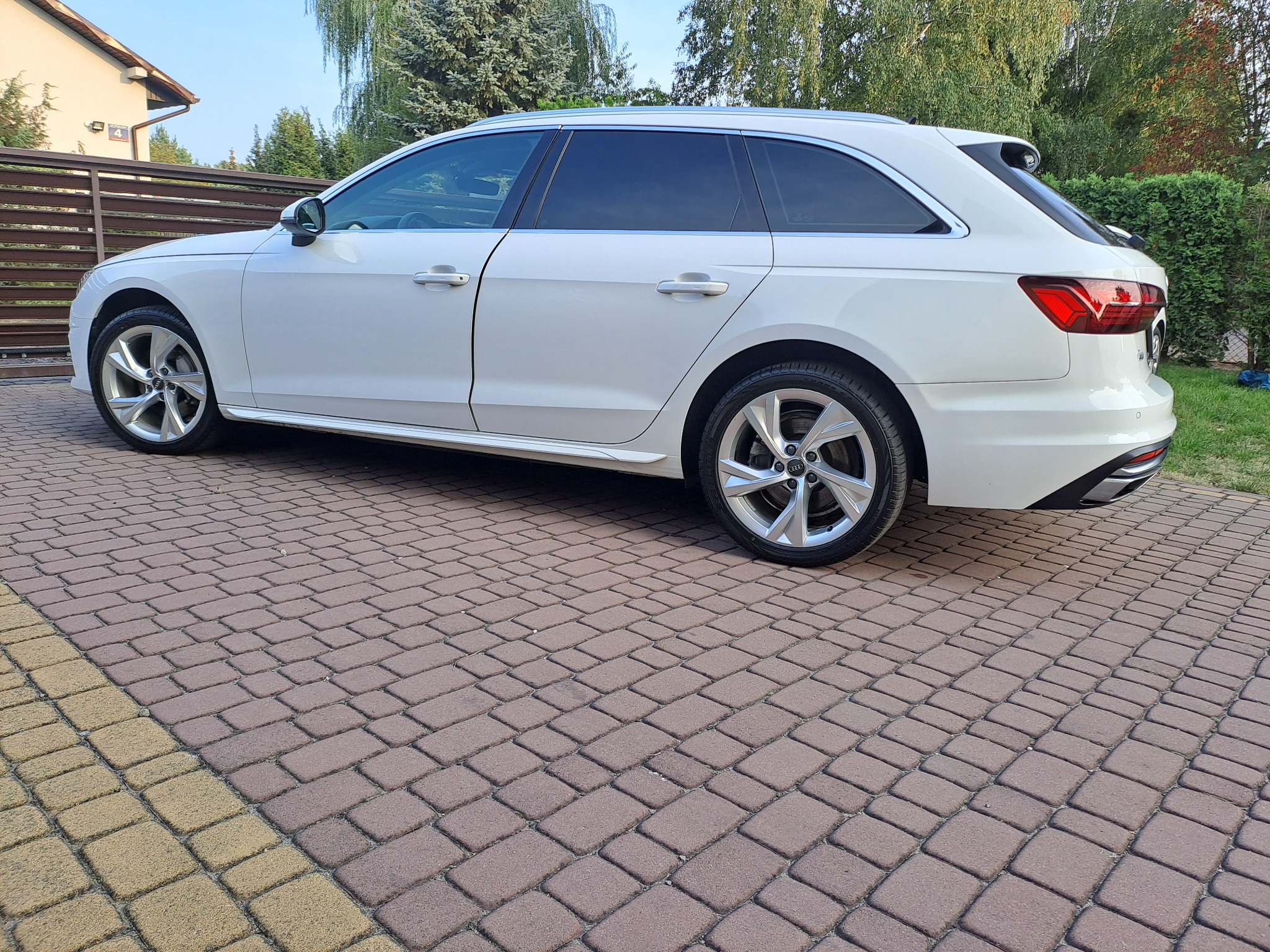 Białe kombi z przyciemnionymi szybami bocznymi i tylnymi, zaparkowane na kostce brukowej w słoneczny dzień.