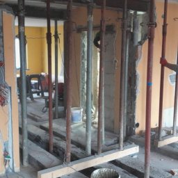 P&m bud - Demontaż ściany działowej w trakcie prac remontowych, widoczne stalowe podpory, instalacja elektryczna w ścianie i pracownik w odzieży roboczej.