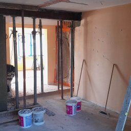 P&m bud - Wnętrze w trakcie remontu: metalowe podpory podtrzymują nadproże, widoczne wiadra z zaprawą, łata murarska oparta o ścianę, przygotowanie do prac wykończeniowych.