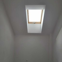 P&m bud - Poddasze po remoncie z oknem dachowym, ściany i sufit w kolorze szarym, widoczne gniazdko elektryczne i fragment podłogi zabezpieczonej folią.