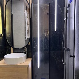 P&m bud - Nowoczesna łazienka z czarnymi marmurowymi płytkami, kabiną prysznicową z podświetleniem LED, owalnym lustrem i drewnianą szafką pod umywalką.