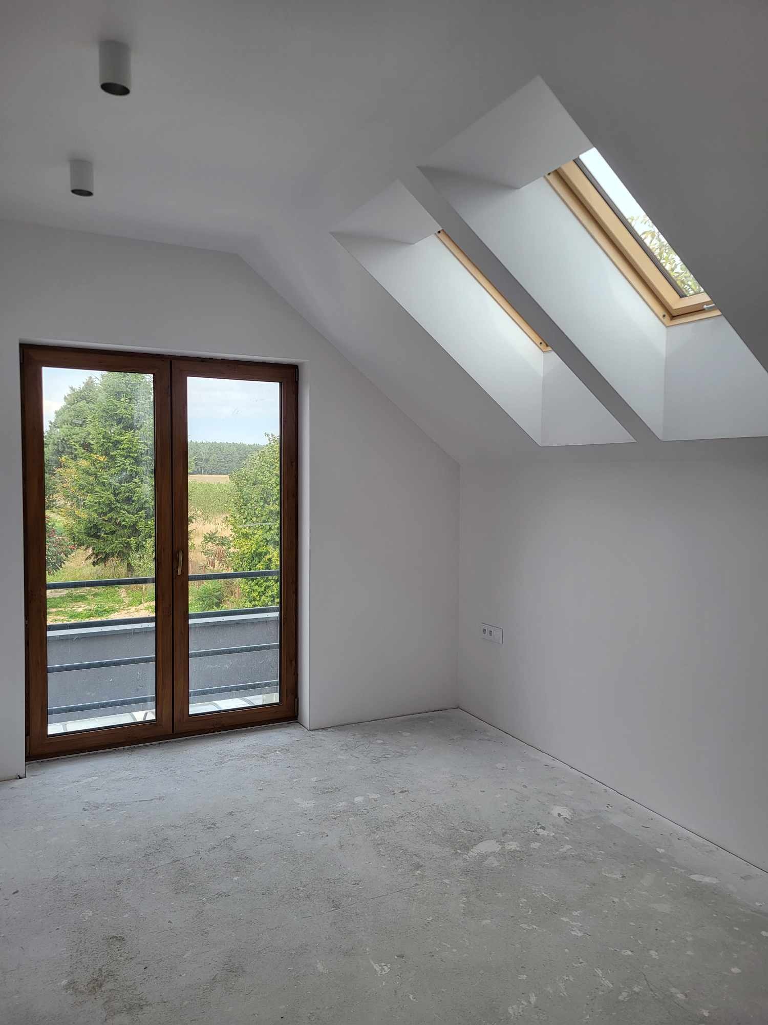 Poddasze w Tomaszowie Mazowieckim z oknami dachowymi i balkonowymi przed wykończeniem, widoczna surowa wylewka podłogowa i świeżo pomalowane ściany na biało.