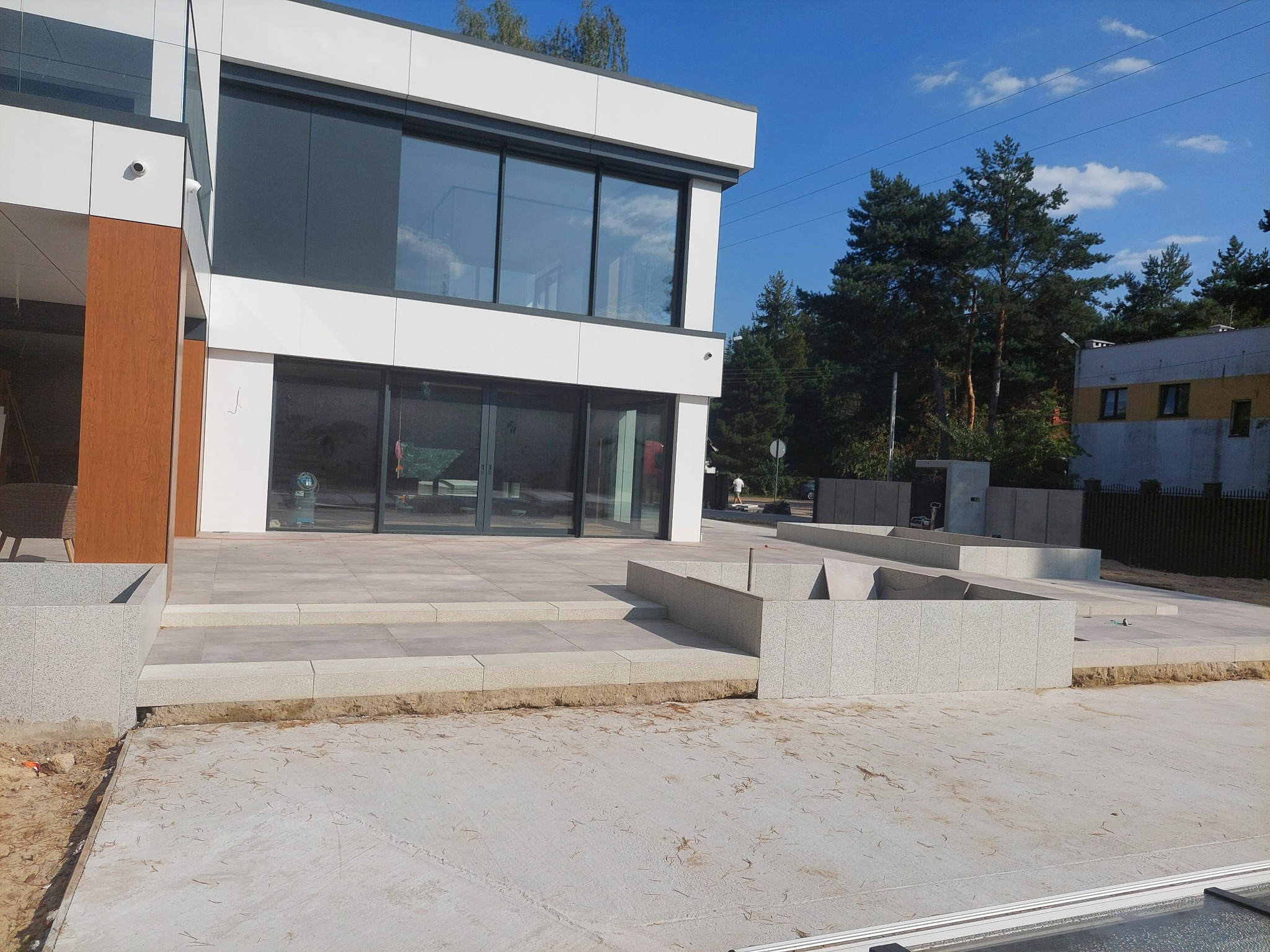 Nowoczesny taras z jasnoszarej kostki granitowej w trakcie budowy, z widocznymi elementami konstrukcyjnymi i fragmentem budynku w tle.