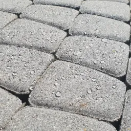 Szara kostka brukowa z kroplami wody na powierzchni, ułożona w regularny wzór.