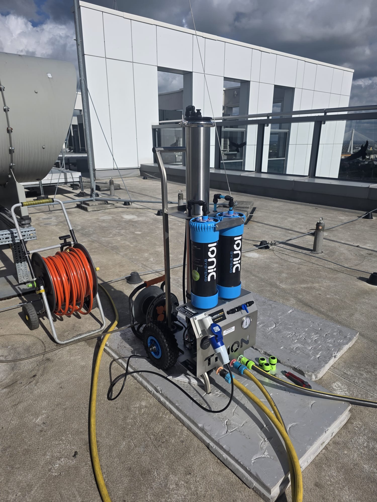 Profesjonalny sprzęt do czyszczenia Ionic Systems na dachu budynku z widoczną zwiniętą pomarańczową rurą i elementami instalacji. Widok na nowoczesną architekturę.