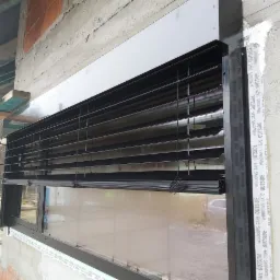 Montaż zewnętrznych żaluzji fasadowych na oknie w surowym stanie wykończenia budynku, widoczne taśmy uszczelniające i rusztowanie w tle.