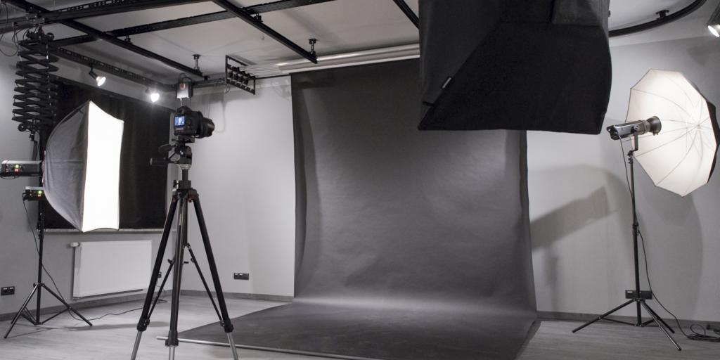 Studio fotograficzne z szarym tłem, lampami błyskowymi i aparatem na statywie, gotowe do sesji.