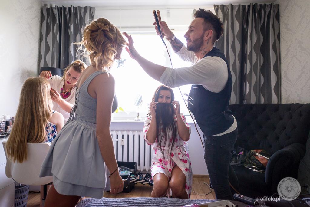 Przygotowania panny młodej: fryzjer stylizuje włosy prostownicą, makijażystka poprawia makijaż, a koleżanka trzyma włosy przed twarzą, udając brodę.