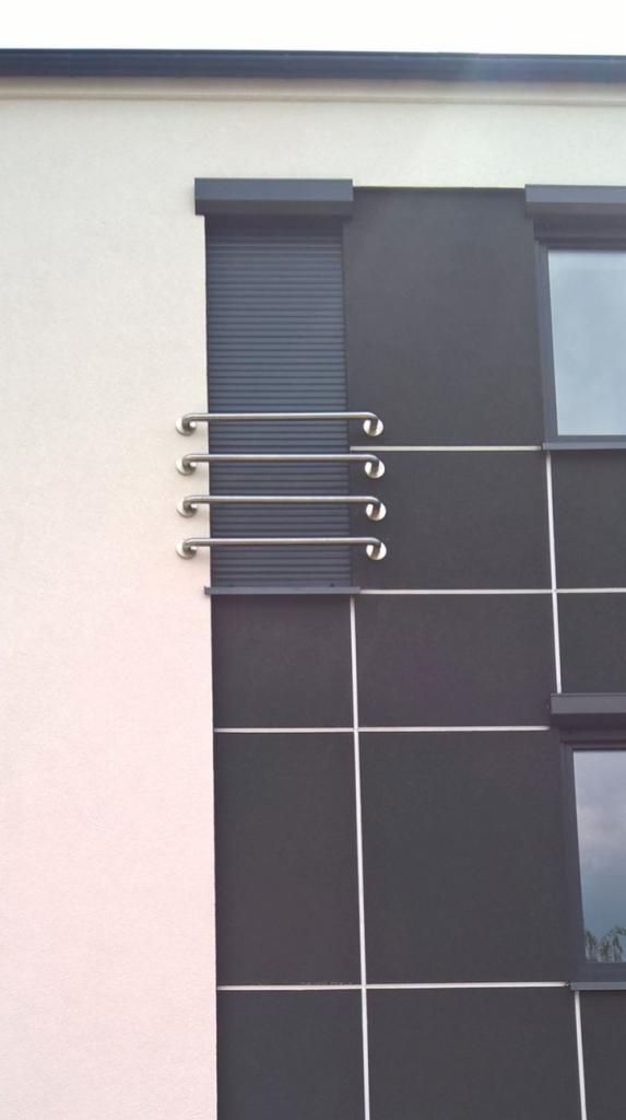 Zewnętrzne, metalowe poręcze przymocowane do elewacji budynku z roletami zewnętrznymi i oknami z podziałami.