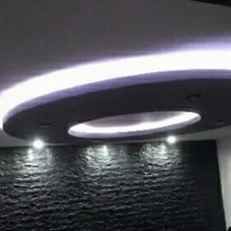 Okrągły, podwieszany sufit z oświetleniem LED w nowoczesnym wnętrzu, ściana wykończona czarną, strukturalną okładziną.